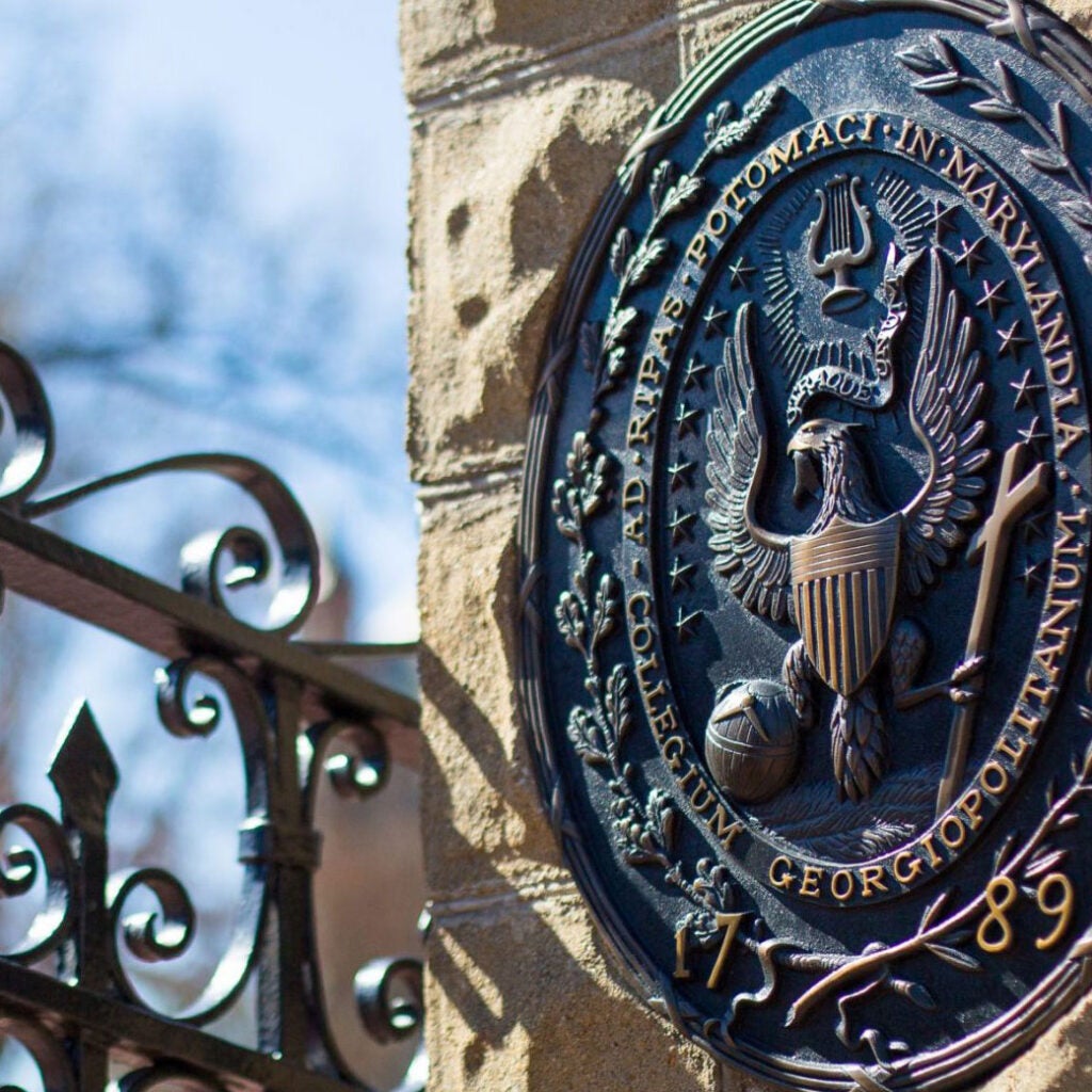 Image of Main Gaet at the entrance of Georgetown University on O street - showing the University Seal on a stone pillar, with part of the iron gate on the left-hand side