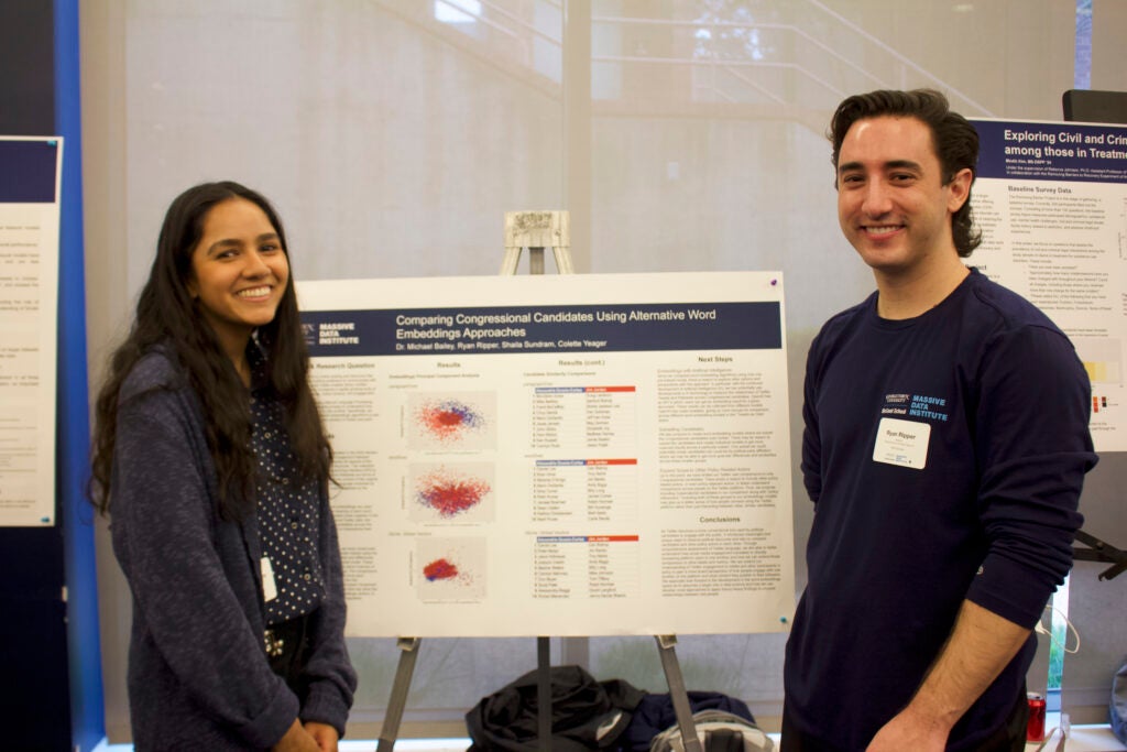 Shaila and Ryan standing, smiling in front of their poster